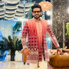 Ready for a wedding ceremony in a stunning red and pink shaded sherwani. The geometric patterns and rich colours make a bold statement, perfect for a grand celebration.