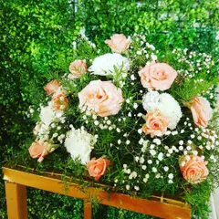 A close-up of a floral arrangement featuring peach roses, white carnations, and baby's breath. These bouquets can be used as centerpieces or accents to complement the main stage decor.
