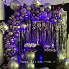 For this celebration, we went with a cool, futuristic vibe. A silver fringe curtain is the backdrop for a balloon arch in shades of metallic purple and silver, accented with star-shaped foil balloons for that extra pop.