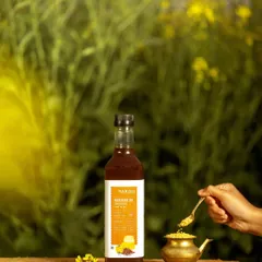 Barosi's mustard oil bottle photographed in a field of yellow mustard flowers. This powerful image creates a direct visual link between the final product and its natural source, emphasizing its purity and origin.