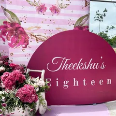 The personalized sign for Theeksha's eighteenth birthday, featuring elegant script against a rich magenta background, complemented by a cart of fresh flowers.