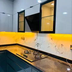 A close-up of a sleek kitchen design with a built-in hob and a modern chimney. The yellow-tinted glass cabinets with internal lighting add a unique, warm accent to the space.