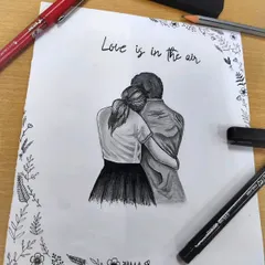 A closer look at the "Love is in the air" couple sketch, showing the fine pencil work and the delicate floral border I added with a pen. My art supplies are always part of the creative process.