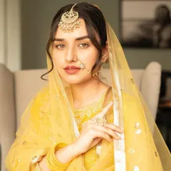 A model styled in a 'Heeramandi' inspired look. The makeup is regal and dewy, with defined eyes, a nude lip, and traditional jewelry like a passa and nath, paired with a soft low bun.