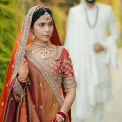 A creative shot of the bride in focus with the groom blurred in the background, building anticipation for the moment they meet at the mandap.