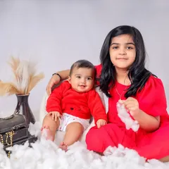 A delightful sibling portrait featuring an older sister and her baby brother. The festive red outfits and dreamy white cloud setup in our studio create a sweet and memorable photograph.
