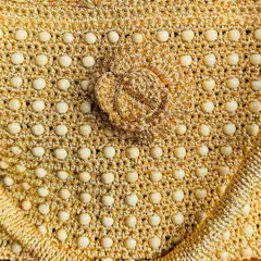 A close-up look at the detailed craftsmanship of the gold beaded bag, showing the texture of the crochet and the carefully placed beads.