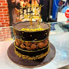 A decadent chocolate cake with a fault line filled with Ferrero Rocher chocolates, topped with a gold "Happy Birthday" sign.
