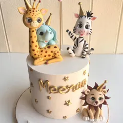 A wild jungle party on a cake. This design features adorable, hand-sculpted safari animals like a giraffe, zebra, and lion, all wearing party hats and surrounded by golden stars for a festive birthday celebration.