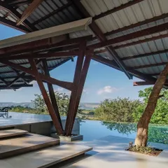 The unique timber frame structure of the Lateral Verandah House marks a natural pause on the sloping hill. This open verandah, overlooking the infinity pool, blurs the line between the built form and the expansive valley beyond, creating a space of tranquil contemplation.