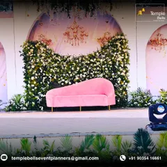 A chic and romantic stage setup perfect for an engagement or reception. A plush pink chaise lounge sits before a backdrop of white flowers and elegant chandelier illustrations, creating a soft and inviting focal point.
