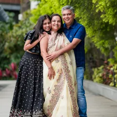 A beautiful family portrait of parents with their teenage daughter. The genuine hug and smiles show the warm bond they share.