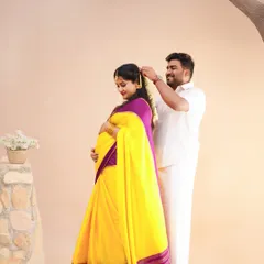 A tender moment during a traditional maternity shoot, where the husband-to-be lovingly places flowers in his wife's hair. She looks radiant in a yellow and purple silk saree.