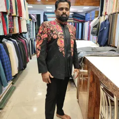 A client trying on a designer black Indo-Western jacket. The piece is adorned with vibrant, multi-colored floral embroidery, making it a showstopper for any festive occasion.