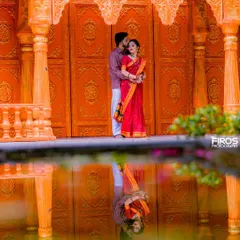 A tender moment captured against a vibrant orange backdrop. The reflection in the water adds a beautiful symmetry to this portrait of a couple in traditional Indian outfits.
