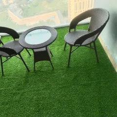 A high-rise balcony in Noida's Supernova Spira tower with a 35mm grass installation. It creates a comfortable seating area with a stunning view.