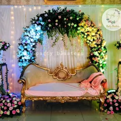 A classic engagement stage design featuring a full floral arch over a vintage-style diwan. The lighting highlights the different colors in the flowers, creating a warm and inviting space for the couple.