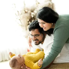 A bright and airy lifestyle newborn session. Here, new parents gaze lovingly at their baby in a relaxed, natural setting filled with soft light and textures.