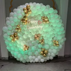 This stunning anniversary backdrop features a full wall of white balloons with elegant gold balloon accents. The "Happy Anniversary" neon sign in the middle glows beautifully, creating a sophisticated and celebratory focal point.