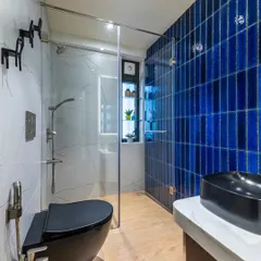 A modern washroom from the Filigree House project. The vibrant blue vertical tiles create a stunning feature wall, contrasted with a sleek black toilet and vessel sink for a bold, contemporary look.