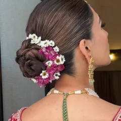 A close up of a sleek, intricately woven bridal bun. I surrounded the base with fresh pink and white daisies for a touch of natural elegance, creating a timeless look for the wedding ceremony.