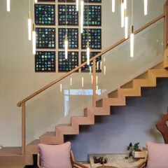 This installation features a grid of twelve abstract paintings, creating a stunning gallery wall next to a modern staircase. Each panel is a unique exploration of texture and color within a cohesive palette of blues and greens.
