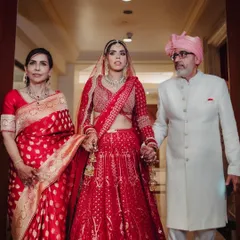 A poignant moment as the bride walks with her parents. Dressed in a classic red lehenga, she holds her father's hand, capturing the emotion and significance of the transition.
