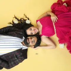 A creative and romantic top-down shot of an expecting couple. The vibrant pink gown and scattered white roses on the yellow background make for a unique and colorful portrait.