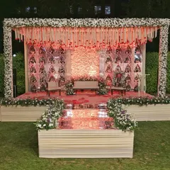 This outdoor reception stage combines traditional elements with modern flair. The design features a floral wall backdrop, intricate hanging decorations, and a beautifully lit platform perfect for photos.