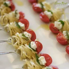 A creative and light appetizer of spaghetti nests with cherry tomatoes and fresh cheese. Each bite sized portion is served on a fork, making it an elegant and easy to eat starter for any sophisticated event.