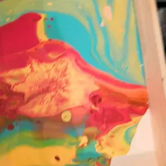 The paint begins to flow across the canvas, with vibrant shades of turquoise, yellow, and red blending together to form a dynamic, flowing landscape.