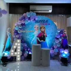 A magical Frozen-themed birthday party for a 4-year-old. This setup includes a custom circular backdrop with Anna and Elsa, life-sized character cutouts, a light-up marquee number, and a balloon arch in a wintery color palette.