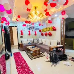 A living room decorated for a welcome surprise with a path of rose petals, red and white balloons, and 'Welcome' foil letters.
