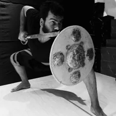 A powerful stance with the 'paricha' (shield) and 'val' (sword). This black and white image captures the intensity of learning ancient Indian weapon skills with our Kalari master.