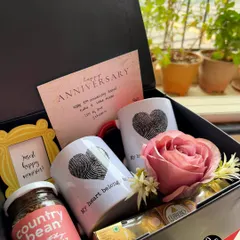 A classic anniversary hamper featuring fingerprint heart mugs, gourmet coffee, a mini photo frame, and a single red rose to say "I love you".