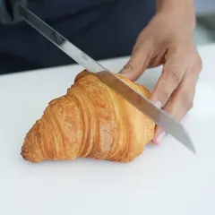 A close-up of a freshly baked croissant being sliced, revealing the delicate, airy layers inside. This is the result of patience, precision, and the right technique.
