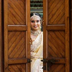 A creative bridal portrait of a South Indian bride peeking through rustic wooden doors, creating a sense of anticipation and charm.