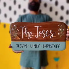 A family name plaque for "The Joses" held with pride. The design combines a rich brown wood stain with a deep teal accent and delicate, hand-painted baby's breath for a touch of class.