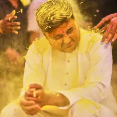 A candid action shot of the groom during the Haldi ceremony, wincing with a smile as he's covered in turmeric paste and petals. These are the fun, real moments you'll want to remember.