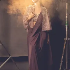Wrapped in elegance, surrounded by mystery. This image captures a model in a beautiful wine-colored cape saree, enveloped in a soft, smoky light.