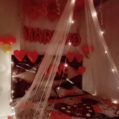 Another view of the romantic room setup, showing the "MARRIED" foil balloons and heart-shaped balloons above the bed. The combination of the sheer canopy and warm lights creates a dreamy and celebratory feel.