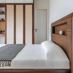 In the compact 'Deux' apartment, we designed this custom hardwood bed with an integrated headboard niche for storage and display. The warm wood tones and clean lines create a cozy, functional, and modern sleeping space for a young couple.