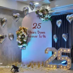 A beautiful setup for a 25th wedding anniversary. It features a personalized backdrop, silver heart-shaped balloons, and a large light-up "25" marquee number.