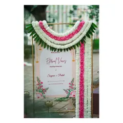 A traditional and elegant welcome to the wedding muhurtham. The sign is framed by a beautiful garland of white and pink flowers, setting a tone of heritage and celebration.