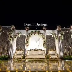 A closer view of the magnificent reception stage. The design features a series of white arches, floral arrangements, and crystal curtains, all reflecting beautifully on the polished golden floor.