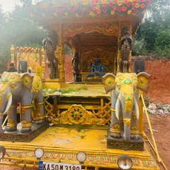 A procession chariot with a deity seated inside, flanked by two decorative elephants and adorned with flowers.