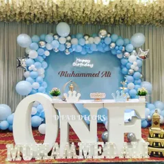 A clean and simple first birthday setup in blue and white. The decor includes a balloon arch, a large "ONE" table, and illuminated marquee letters, perfect for a classic celebration.
