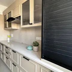 A newly installed kitchen in Nirala Estate, featuring off-white paneled cabinets, sleek black handles, and fluted glass upper cabinets for a touch of elegance.