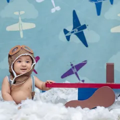 This sitter session features a little pilot in an aviator hat, sitting among fluffy clouds with a toy plane, against a backdrop of vintage aircraft.