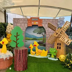 We built a charming countryside scene for Divik's duck-themed first birthday. The setup included a custom stone-arch backdrop showing a pond, a wooden windmill, and adorable 3D duck and frog characters for the little ones to enjoy.